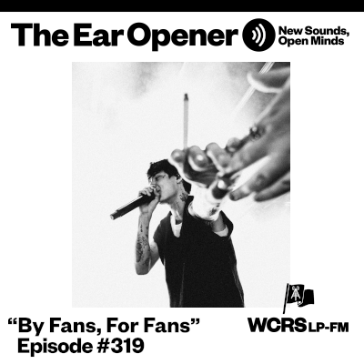 Singer holding out their hand to a fan while he sings. He is holding a cigarette.